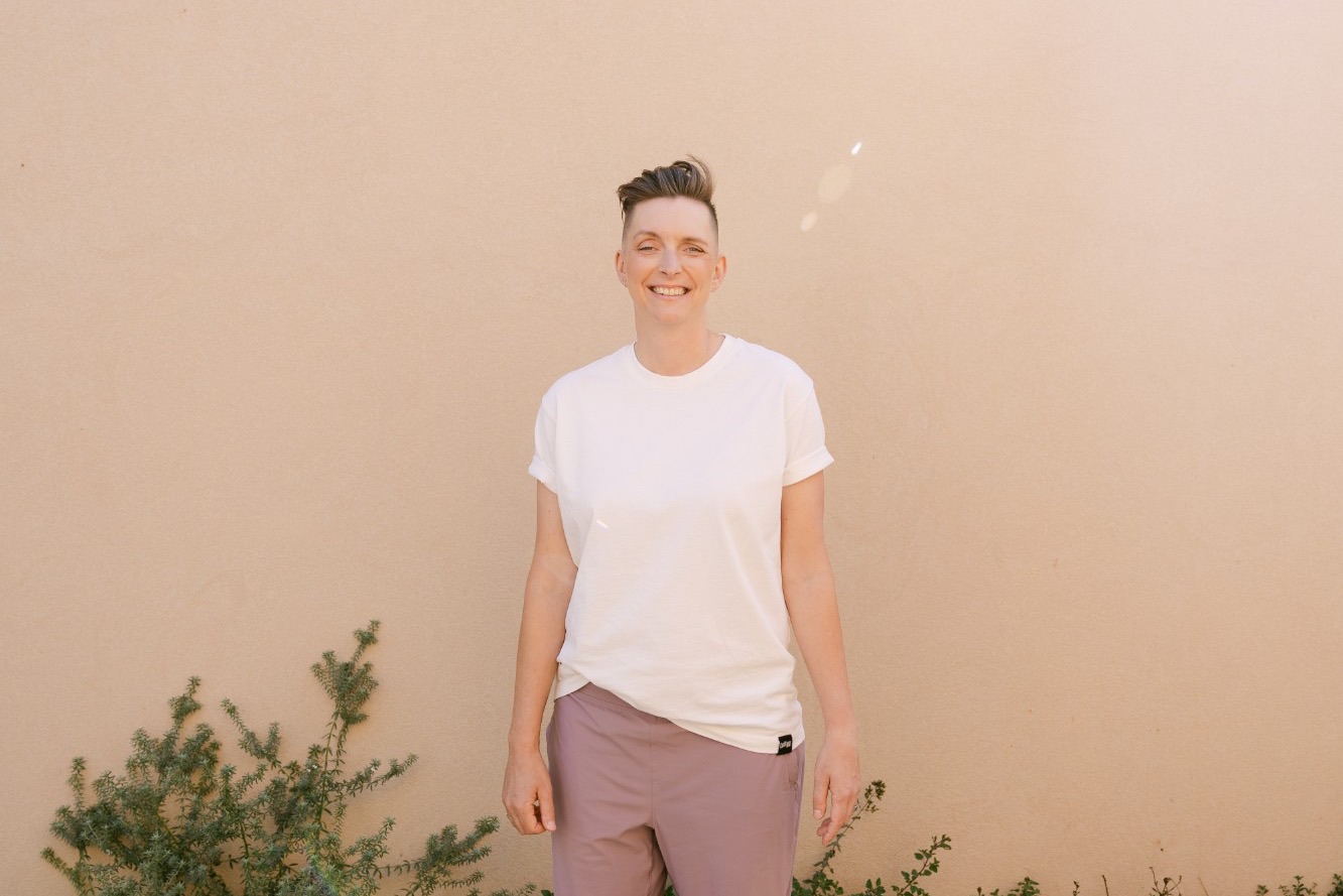 Conni smiling, standing in front of a warm peach wall with green plants